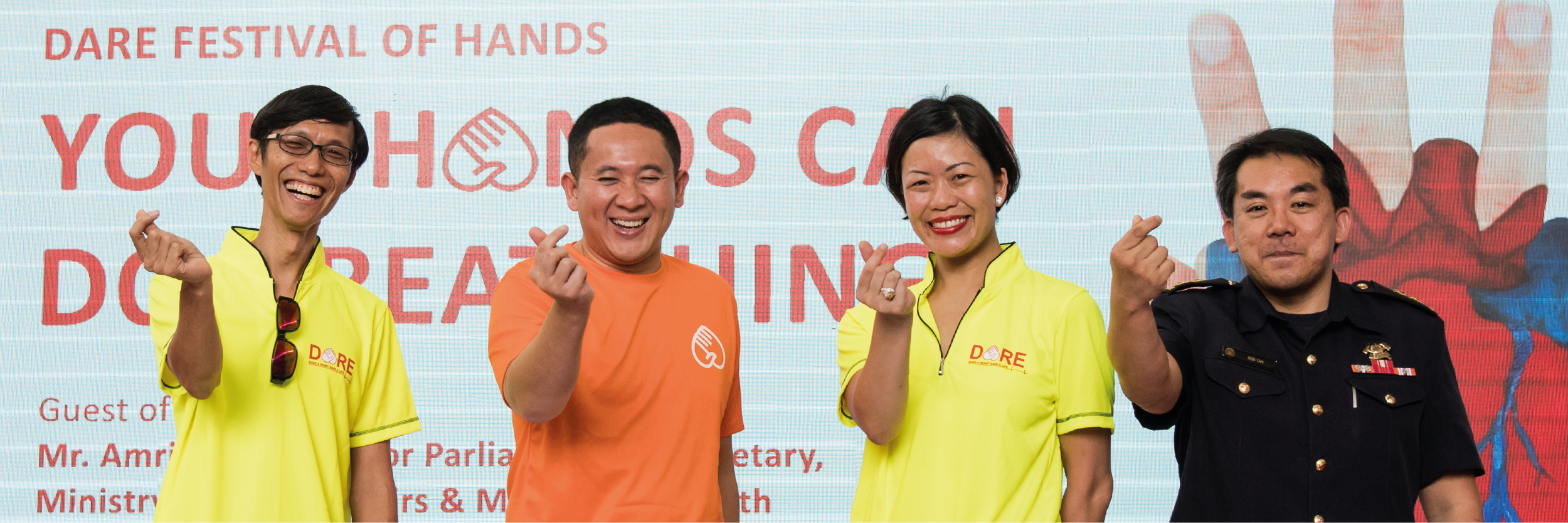 Photo of Professor Marcus Ong, then-Senior Parliamentary Secretary of Health and Home Affairs Mr Amrin Amin, Dr Jade Kua, and SCDF Senior Officer COL Bob Tan making ‘Korean finger hearts’ at the 2018 DARE Festival of Hands campaign.